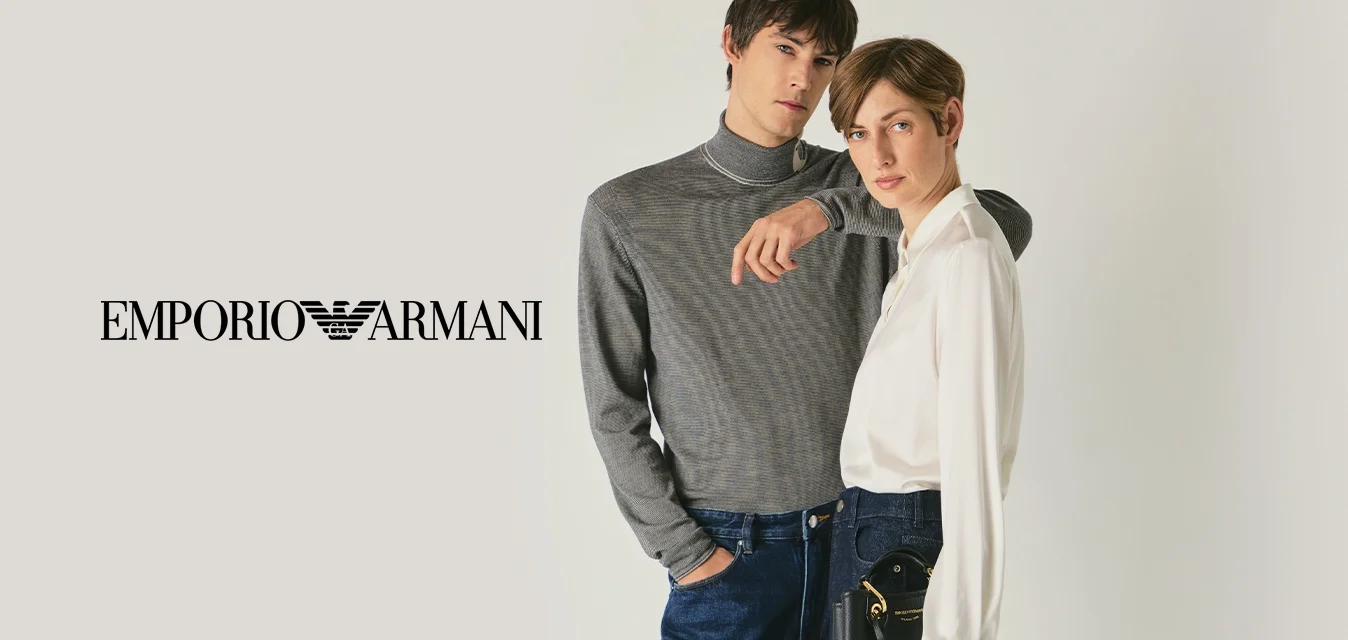 Due modelli stanno vicini; uno indossa un maglione grigio a motivo e jeans, l'altro indossa una blusa bianca, pantaloni larghi scuri e tiene una pochette nera.