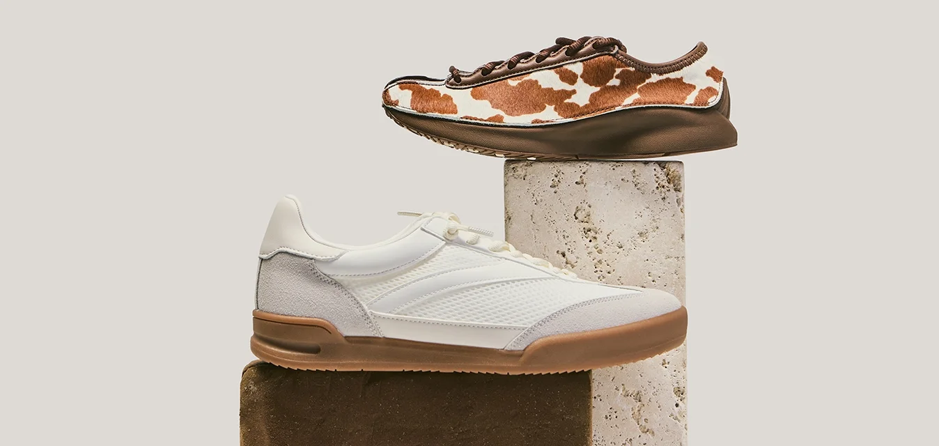 Due sneaker casual esposte su blocchi rettangolari impilati; una bianca con suola marrone chiaro, l'altra marrone con motivo a macchie bianche da mucca.