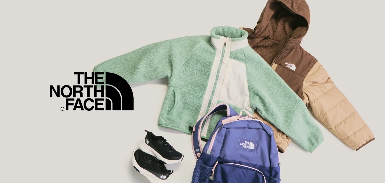 Giacca in pile verde, giacca imbottita marrone e beige, zaino blu e scarpe da ginnastica nere disposti su uno sfondo chiaro.