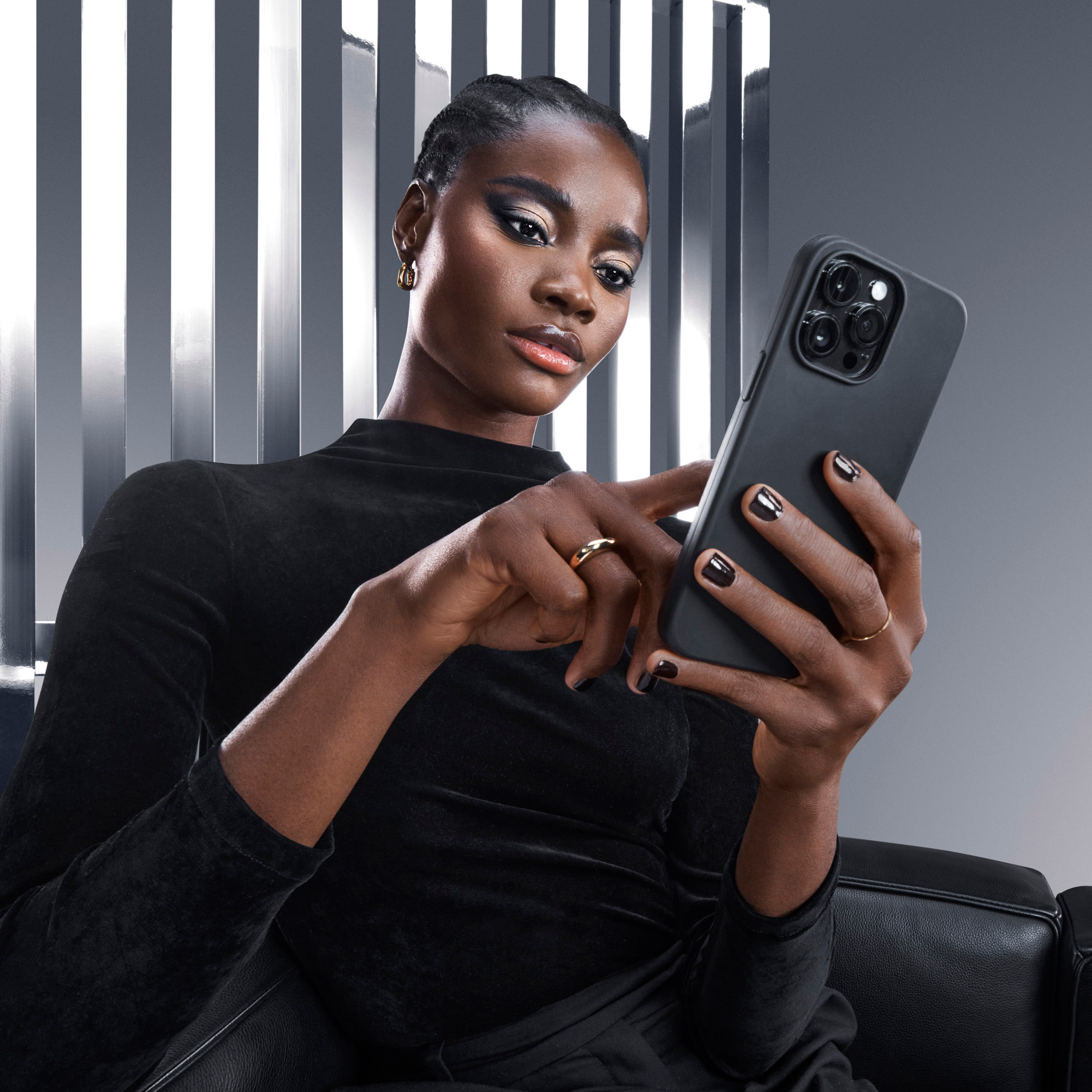 Donna elegante in abito nero con in mano uno smartphone, in un ambiente moderno e minimal.