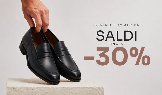 Black leather men's loafers held by a hand on a stone pedestal beside 'Saldi -30%' spring/summer sale text