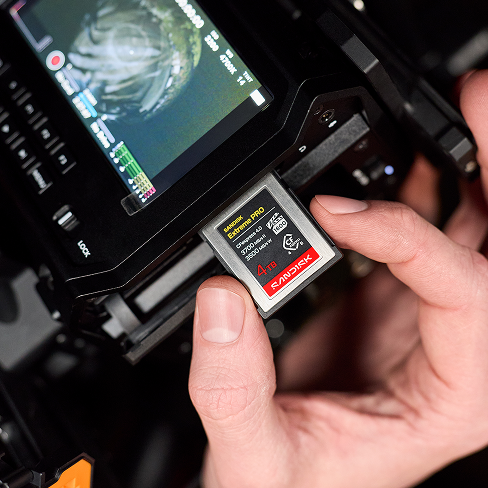 Primo piano delle mani che caricano una scheda SANDISK Extreme PRO CFexpress in una videocamera professionale per una registrazione ad alta risoluzione.