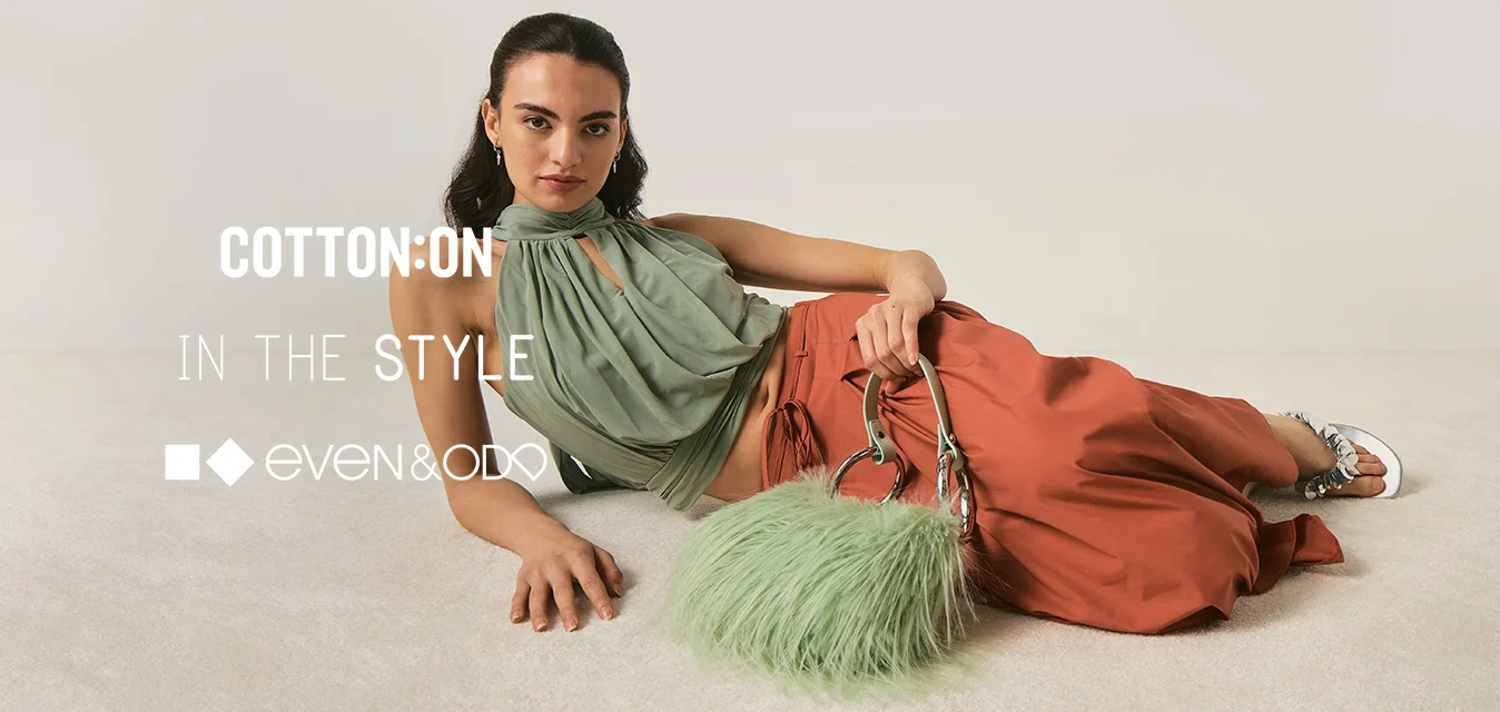 Donna sdraiata a terra che indossa un top verde con collo a halter e pantaloni ampi color ruggine, che tiene in mano una borsa verde soffice con manici argentati.