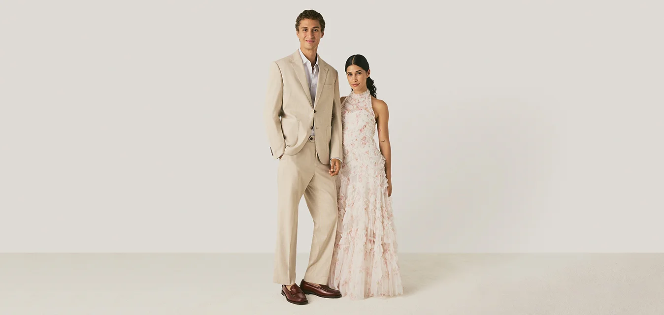 Giovane uomo in completo beige e giovane donna in abito bianco floreale senza maniche stanno uno accanto all'altra contro uno sfondo chiaro uniforme.
