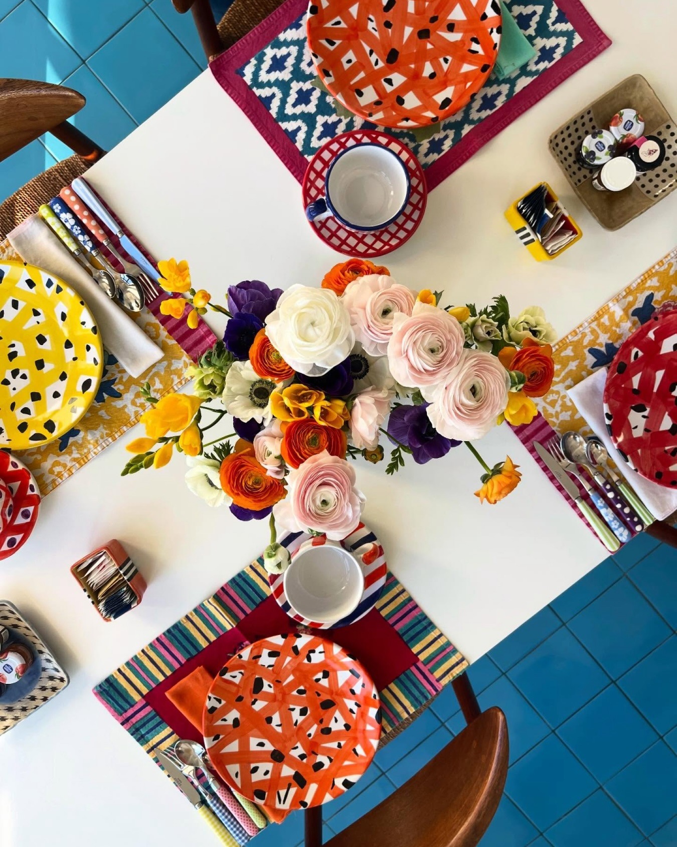 Top-down view of a colourful table setting with patterned plates and a vibrant ranunculus floral centrepiece