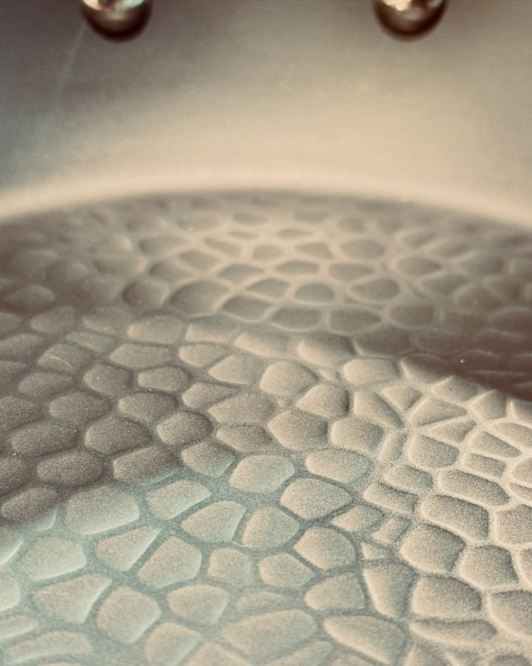 Close-up of textured metallic surface with pebble-like honeycomb pattern, soft shadowing and warm lighting
