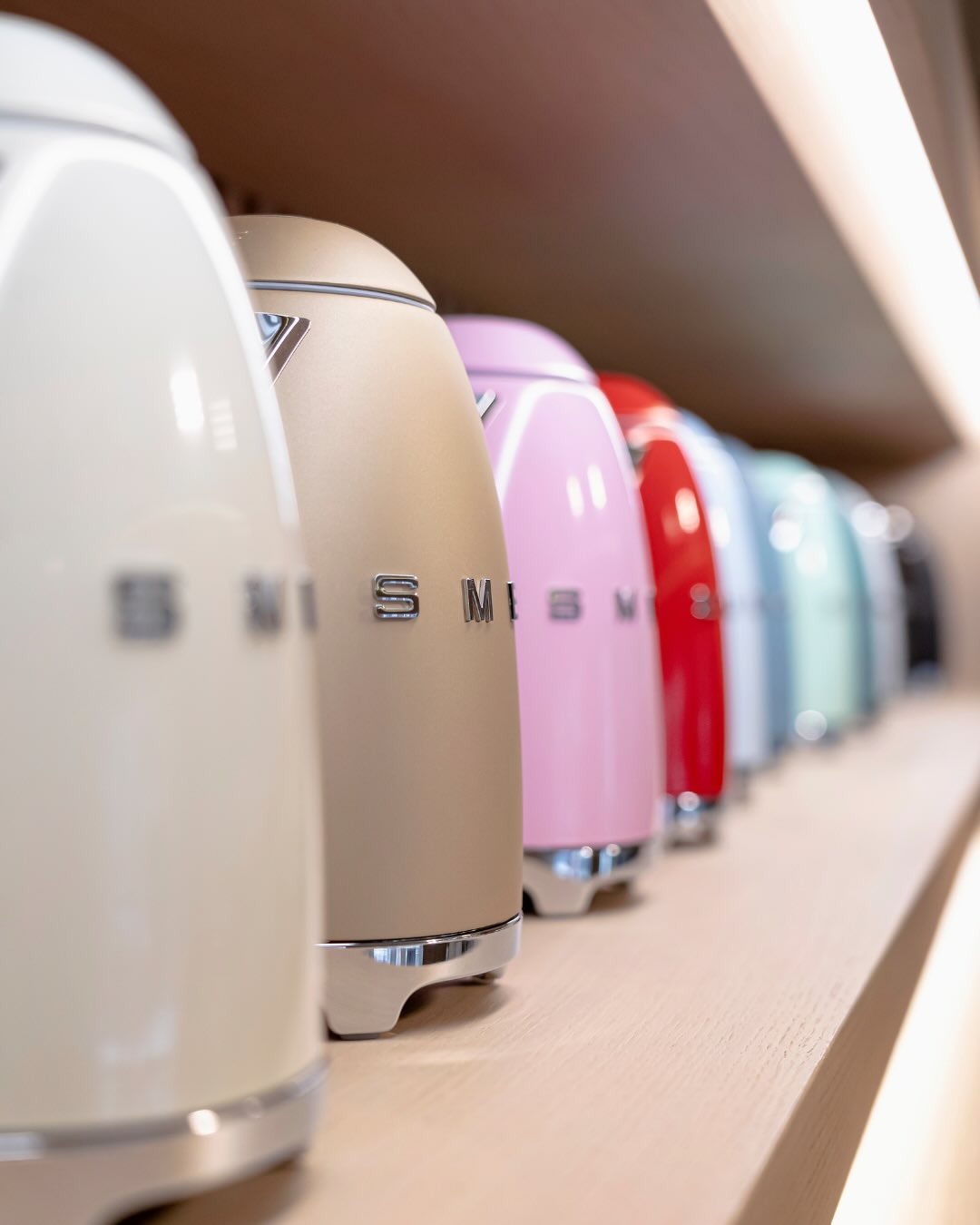Row of pastel and bright retro-style electric kettles on a wooden shelf, close-up with shallow depth of field
