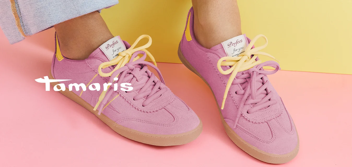 Persona che indossa scarpe da ginnastica rosa con lacci gialli e jeans azzurri seduta su una forma geometrica gialla su un pavimento rosa.