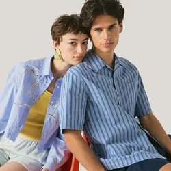 Due persone sedute vicino su una sedia rossa, una indossa una camicia a righe blu e pantaloncini scuri, l’altra una camicia azzurro chiaro con pantaloncini bianchi.