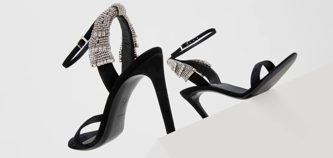 Sandali con tacco alto in suede nero con un design a strisce, caratterizzati da una fascia adornata con strass attorno alla caviglia e punta aperta.