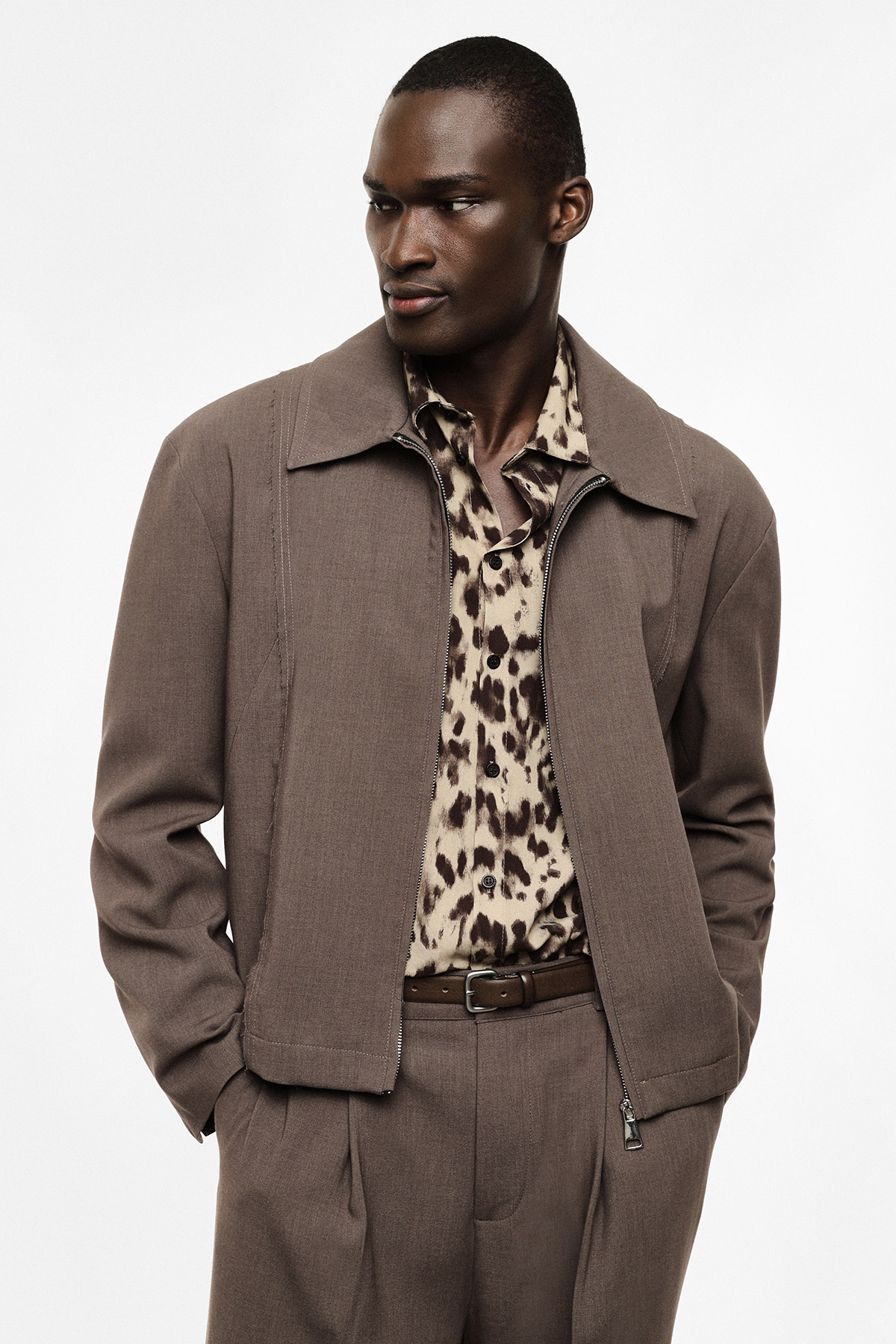 Male model wearing brown tailored jacket and trousers with leopard-print shirt, hands in pockets, looking to left