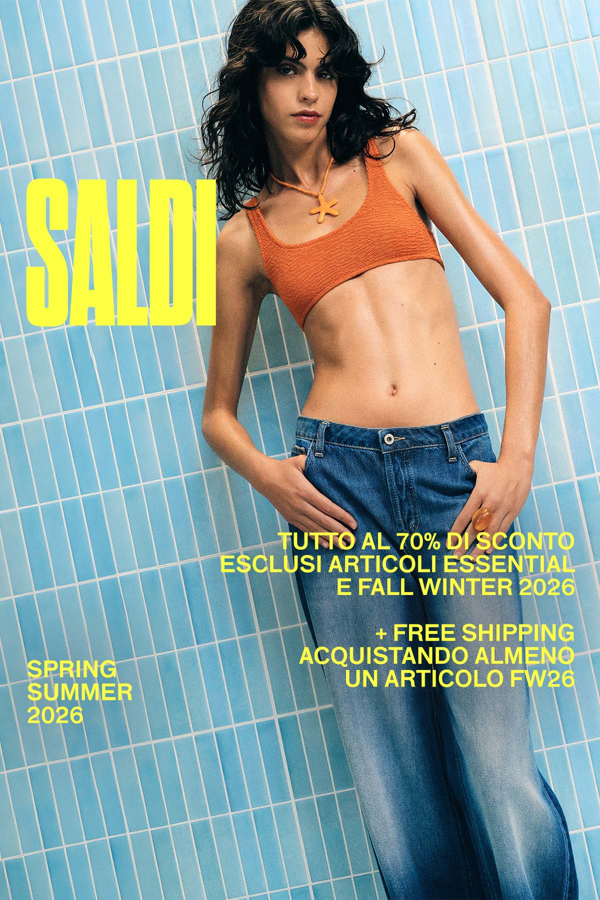 Model wearing an orange crochet crop top and relaxed blue jeans against a pale blue tiled wall with bold yellow "SALDI" sale text