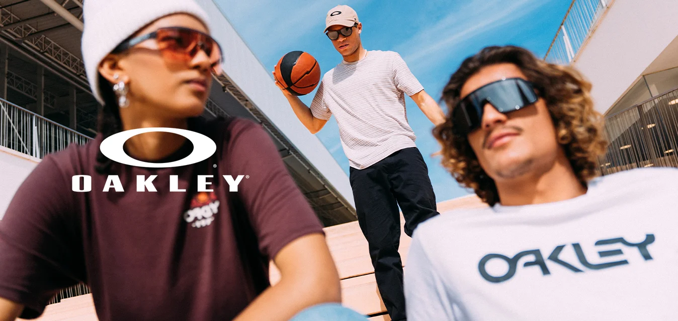 Tre giovani all'aperto sulle scale, uno tiene una palla da basket, tutti indossano occhiali da sole e abbigliamento casual streetwear sotto un cielo azzurro e limpido.