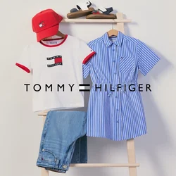 Cappellino rosso, maglietta bianca, jeans blu, vestito blu a righe e sandali esposti su una scala di legno contro un muro semplice.