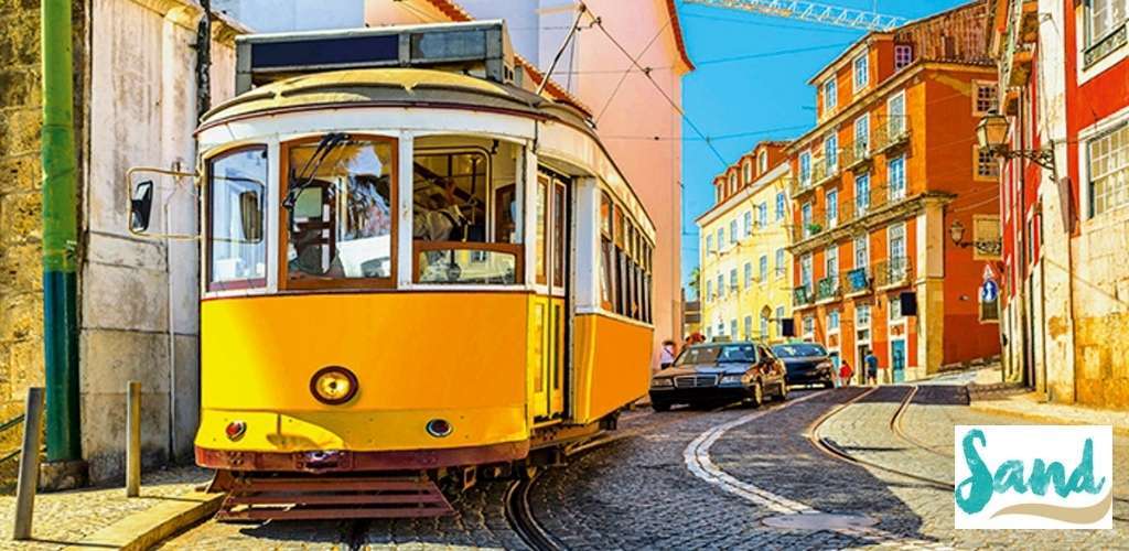 Yellow historic tram on a cobbled Lisbon street with colourful pastel buildings, parked cars and a clear blue sky