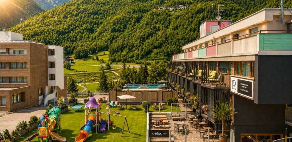 Sunlit mountain resort with outdoor pool, colourful children's playground and terrace seating overlooking a green valley