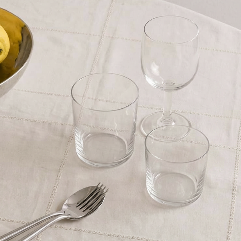 Three clear glasses and silverware are on a white tablecloth.