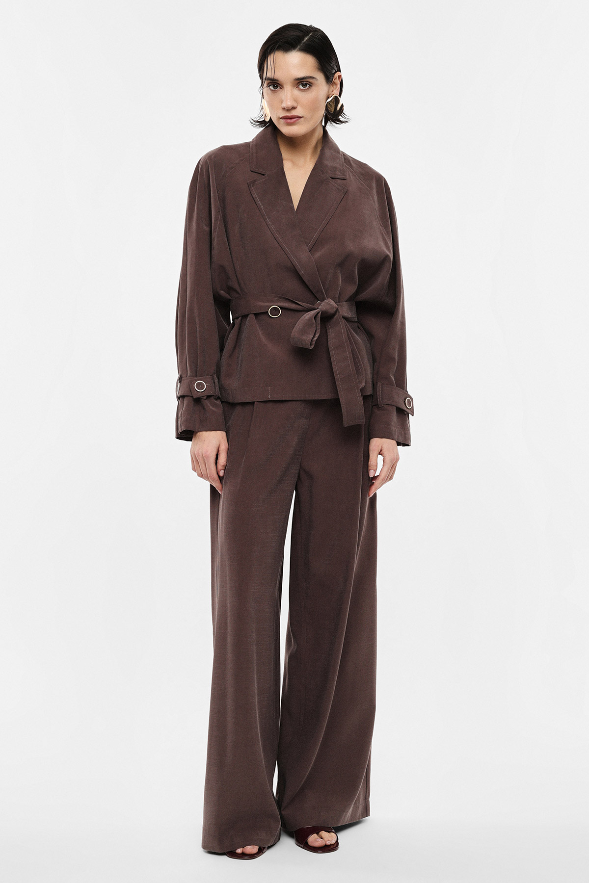 Woman modelling a brown belted blazer and wide-leg trousers on a white studio background
