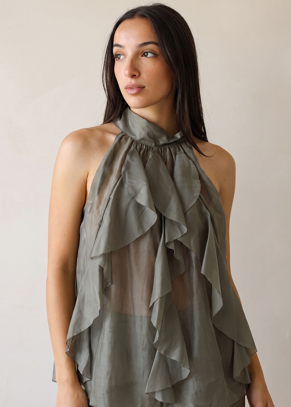 Young woman modelling olive-green sheer ruffled halter blouse against a neutral background