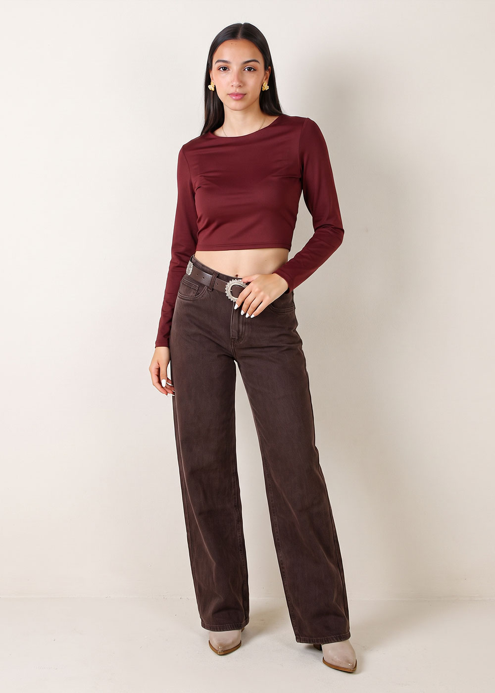 Model wearing burgundy long-sleeve cropped top and brown wide-leg jeans with a statement belt on a neutral background