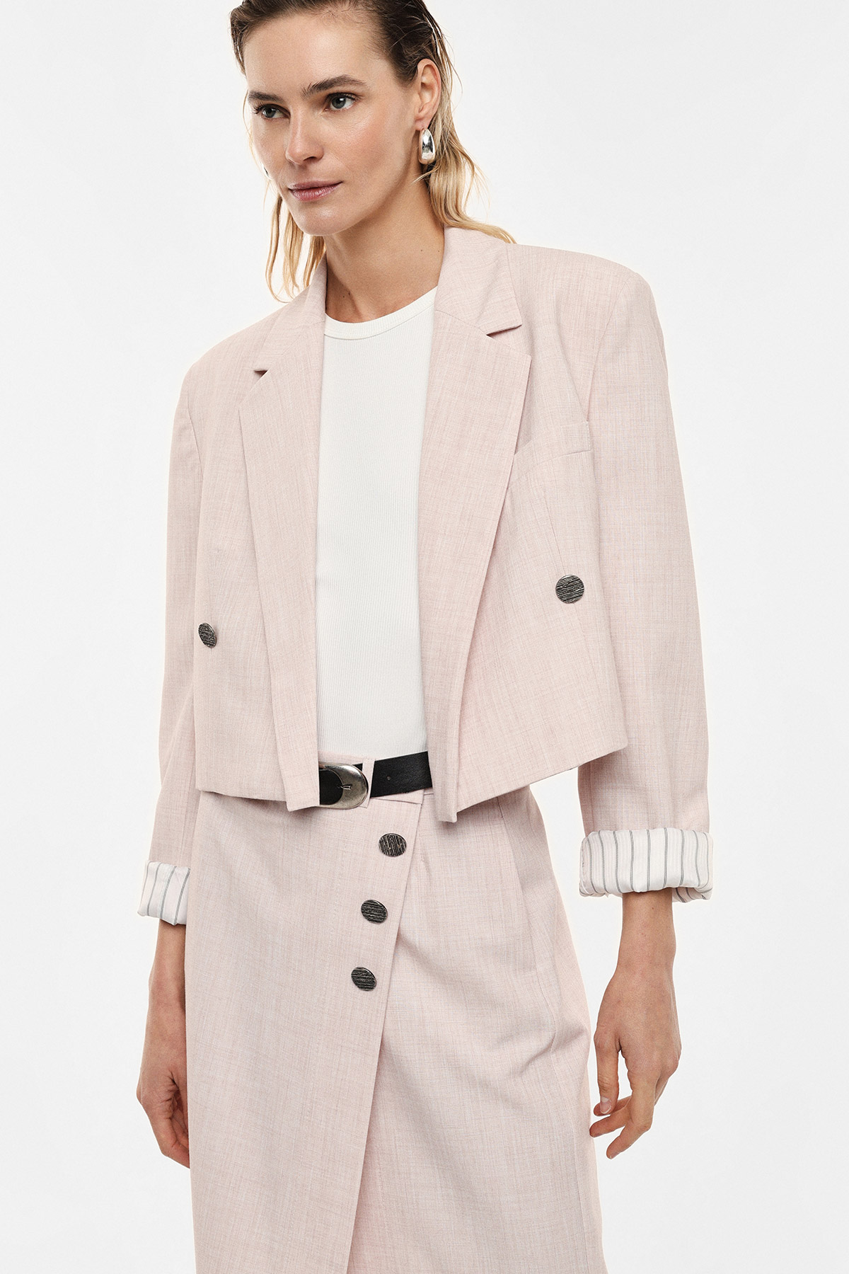 Model wearing pale pink cropped blazer and matching buttoned midi skirt with white top, black belt and silver hoop earrings
