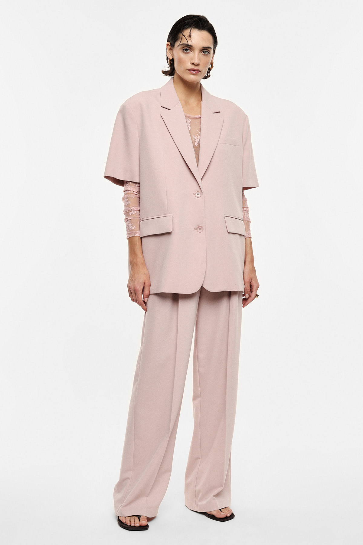 Woman model wearing a pale pink oversized short-sleeve blazer and wide-leg trousers with a lace top and sandals