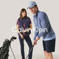 Uomo e donna che si preparano a giocare a golf al chiuso con mazze da golf e una sacca da golf su uno sfondo neutro.