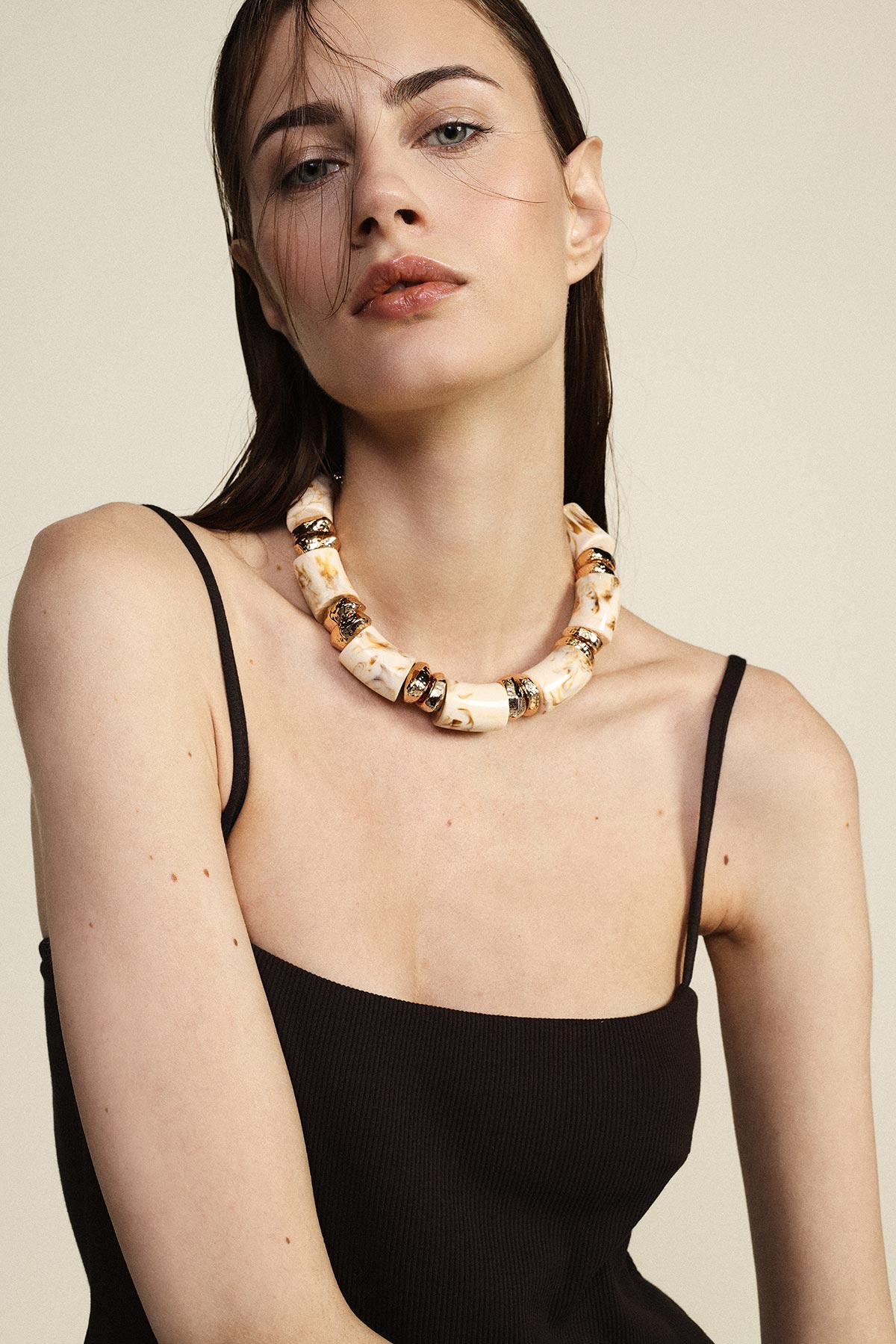 Close-up of a woman wearing a chunky cream and gold statement necklace with a black spaghetti-strap top on a neutral background