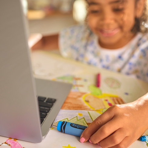 Primo piano di un bambino sorridente che inserisce un'unit&agrave; flash USB-C SANDISK Crayola blu ceruleo nel laptop circondato da carta e pastelli colorati.
