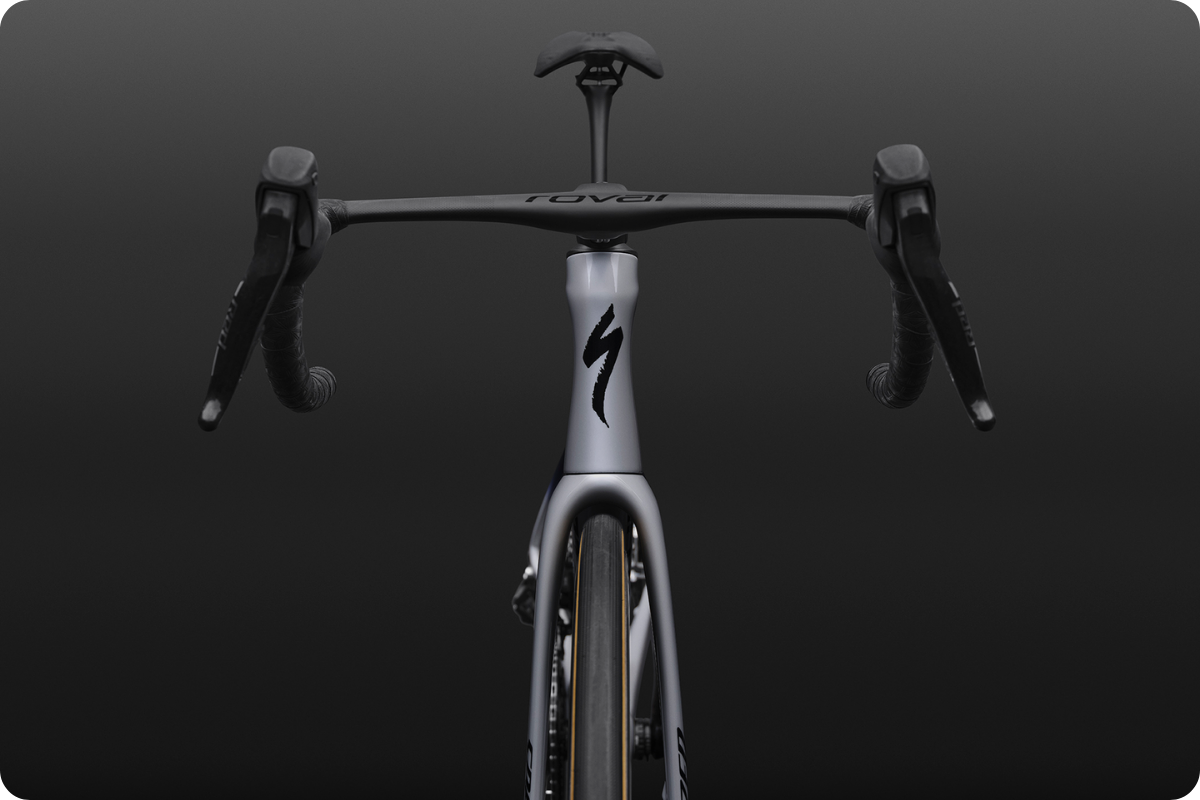 Front view of a modern grey road bike showing drop handlebars, slim fork and tyre against a dark gradient background