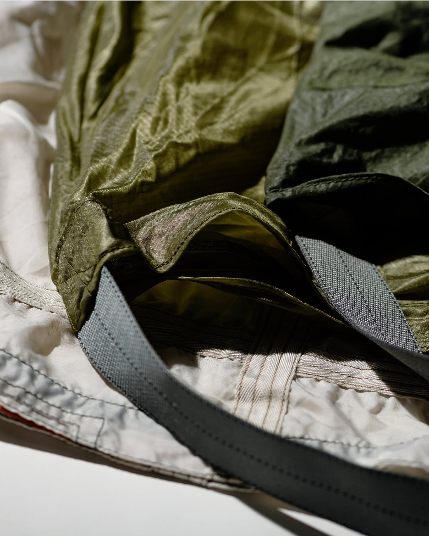 Close-up of olive-green ripstop jacket or sleeping bag fabric with grey webbing strap and white quilted lining
