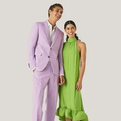 Un uomo in un abito viola chiaro e una donna in un abito senza maniche verde brillante stanno sorridendo contro uno sfondo chiaro e semplice.