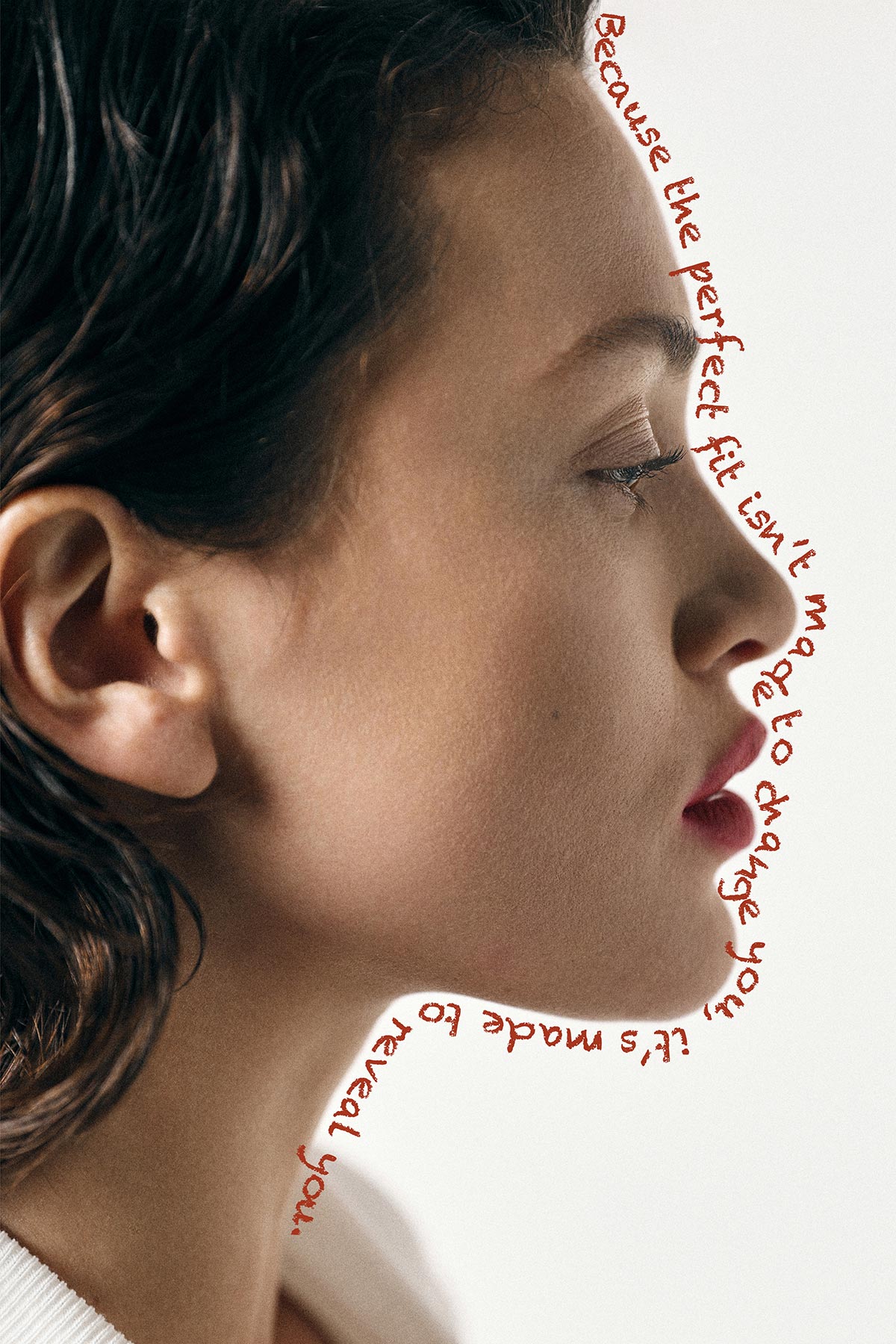 Close-up profile of a woman's face with red handwritten slogan along her jawline about a perfect fit revealing you, beauty portrait