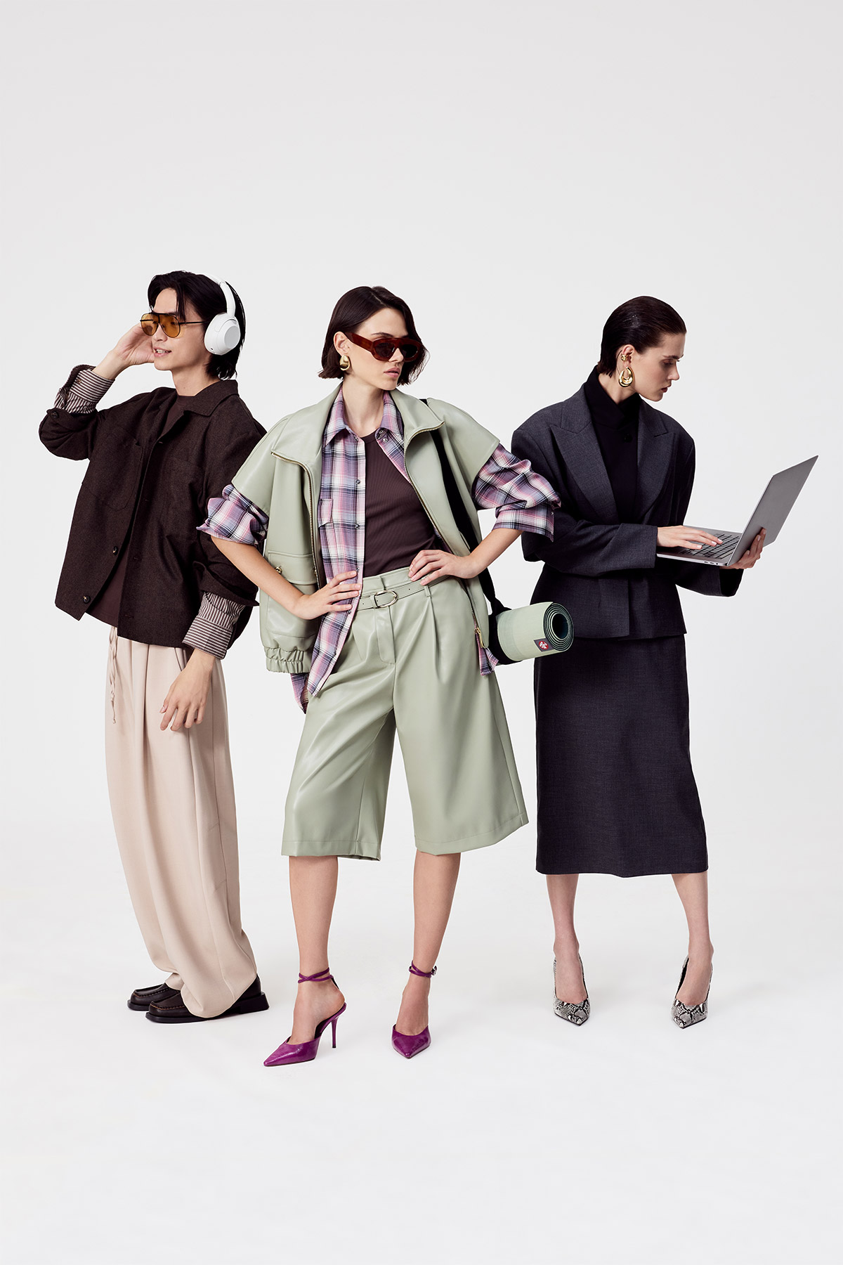Three stylish women modelling contemporary outfits: casual trousers with headphones, pastel green shorts set with sunglasses, and a tailored dark skirt suit with a laptop