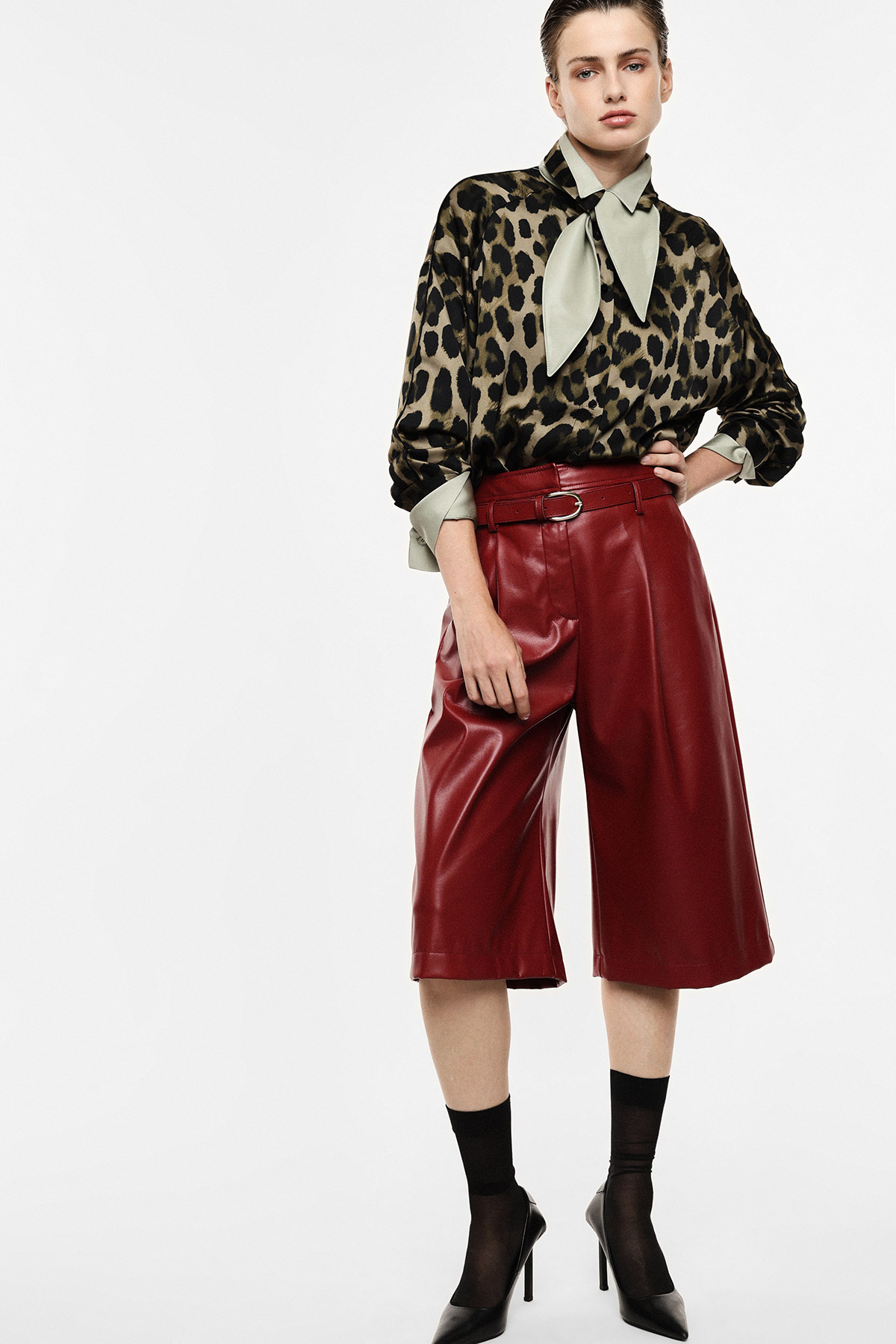 Female model wearing leopard-print blouse with pussy-bow and high-waisted burgundy leather Bermuda shorts with black heels