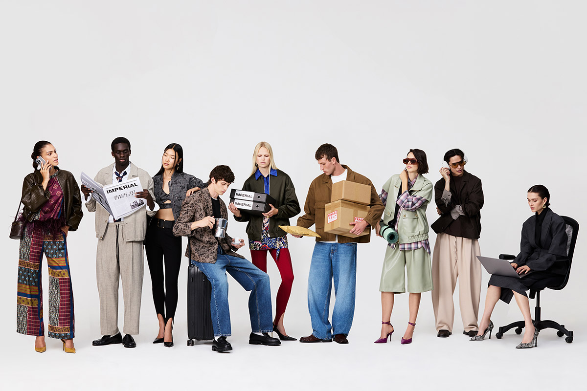 Group of diverse models in contemporary fashion outfits in studio, posing with newspaper, luggage, coffee, boxes and a laptop