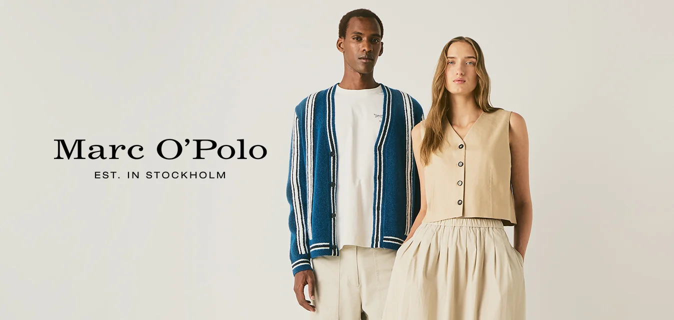 Un uomo con pantaloni chiari, camicia bianca e cardigan a righe blu sta accanto a una donna con top beige senza maniche e gonna lunga con scarpe da ginnastica.