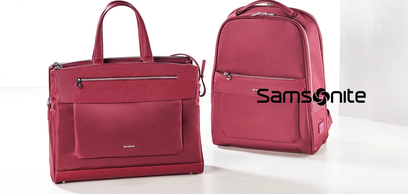 Zaino e borsa a tracolla in tessuto borgogna. Entrambi hanno zip, doppi manici e tasche frontali. Texture liscia con accenti di branding minimi.