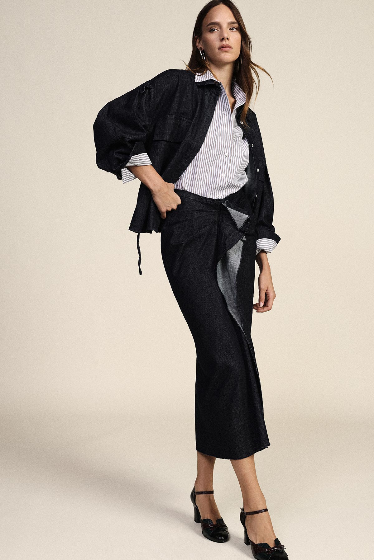 Woman modelling dark denim jacket and wrap midi skirt with striped shirt and black heels on neutral background
