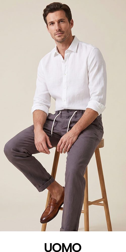 Man seated on stool wearing white linen shirt, grey drawstring trousers and brown leather loafers on neutral background