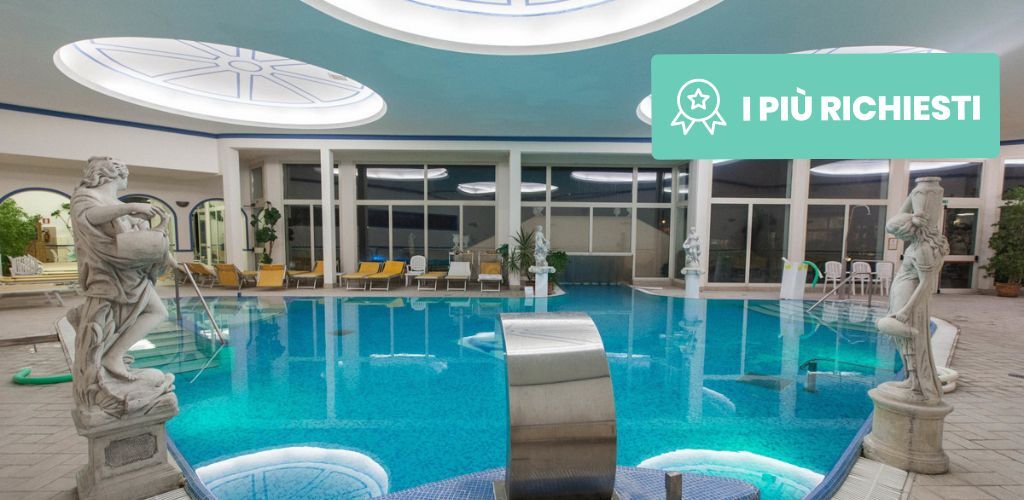 Indoor hotel spa pool with turquoise water, classical marble statues, lounge chairs and large circular skylights