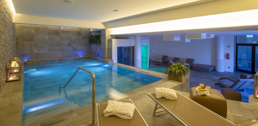 Indoor spa pool with steps and stainless-steel handrail, loungers with folded robes, candles and soft ambient lighting in a modern hotel wellness area