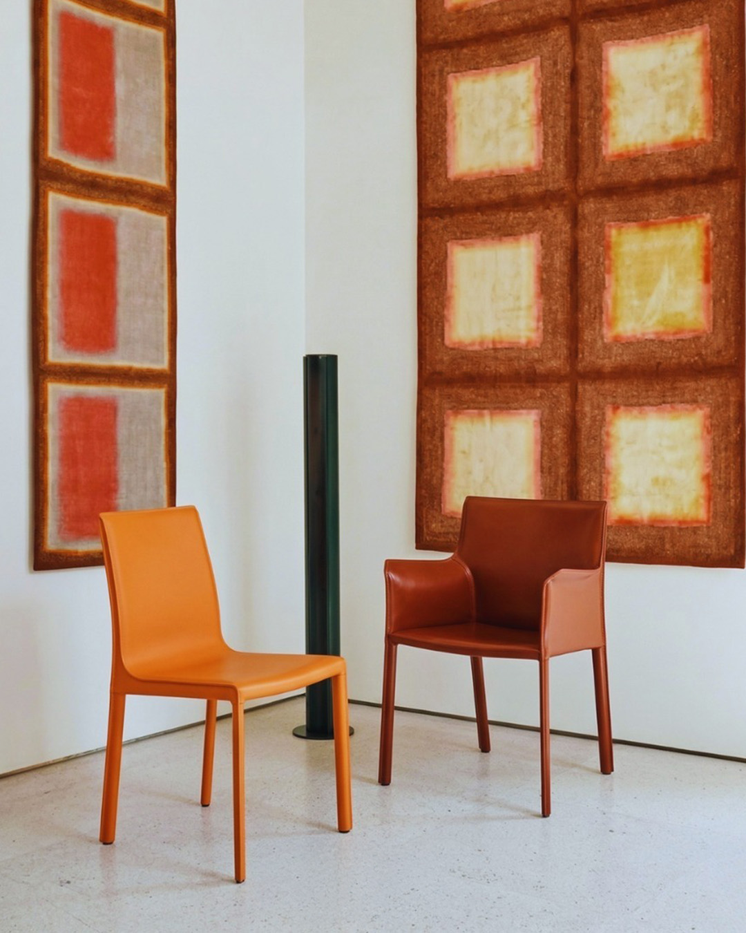 Two modern orange leather chairs in a minimalist gallery setting with abstract square wall art on white walls and pale terrazzo floor