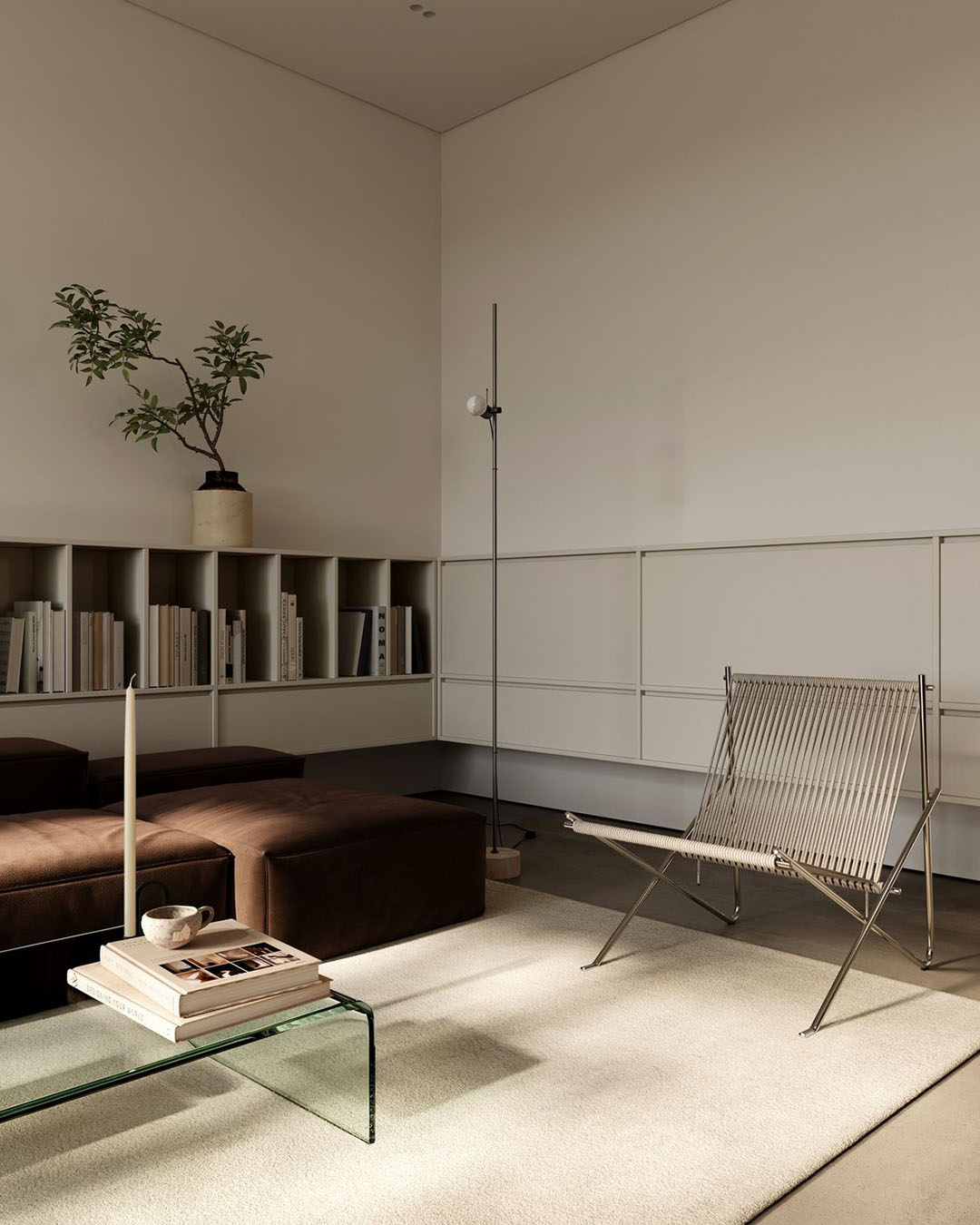 Minimal modern living room with brown ottoman, glass coffee table, woven chair, low bookshelf, floor lamp and potted plant