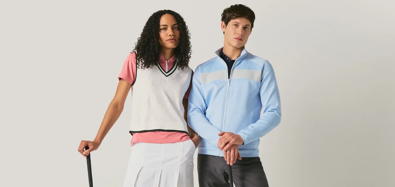 Due golfisti, una donna con gonna bianca e gilet, un uomo con giacca blu e pantaloni neri, in piedi con mazze da golf su uno sfondo uniforme.