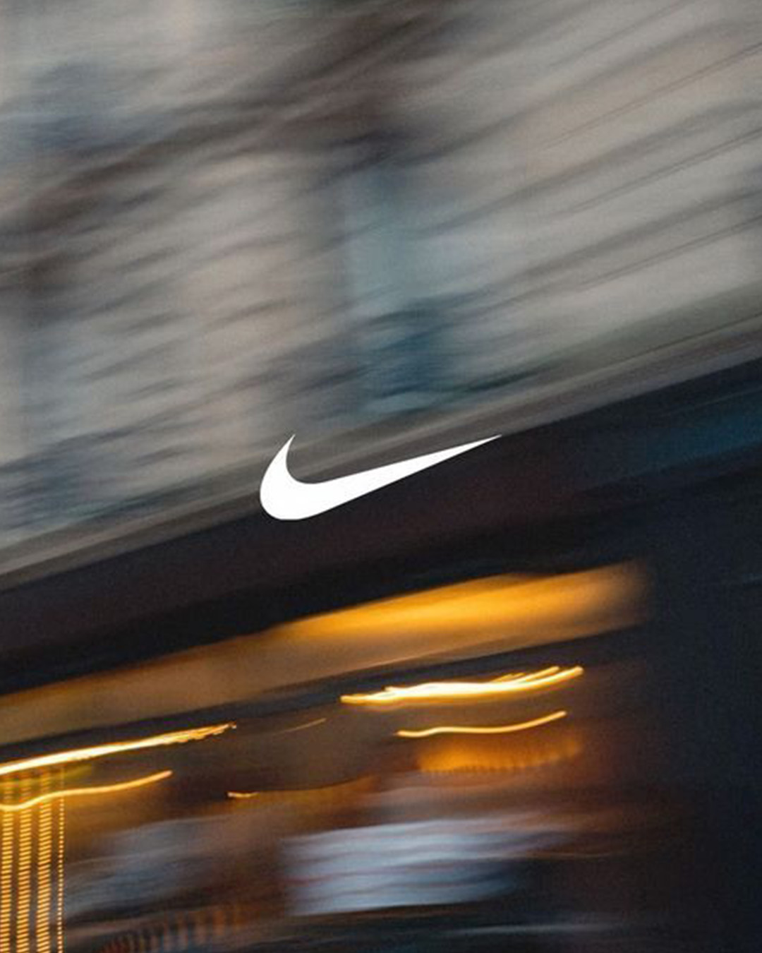 White Nike swoosh logo centred over a blurred urban storefront with warm yellow lights