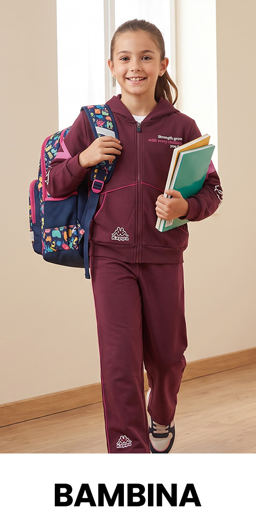 Smiling schoolgirl in maroon tracksuit carrying colourful backpack and books, walking indoors against neutral background