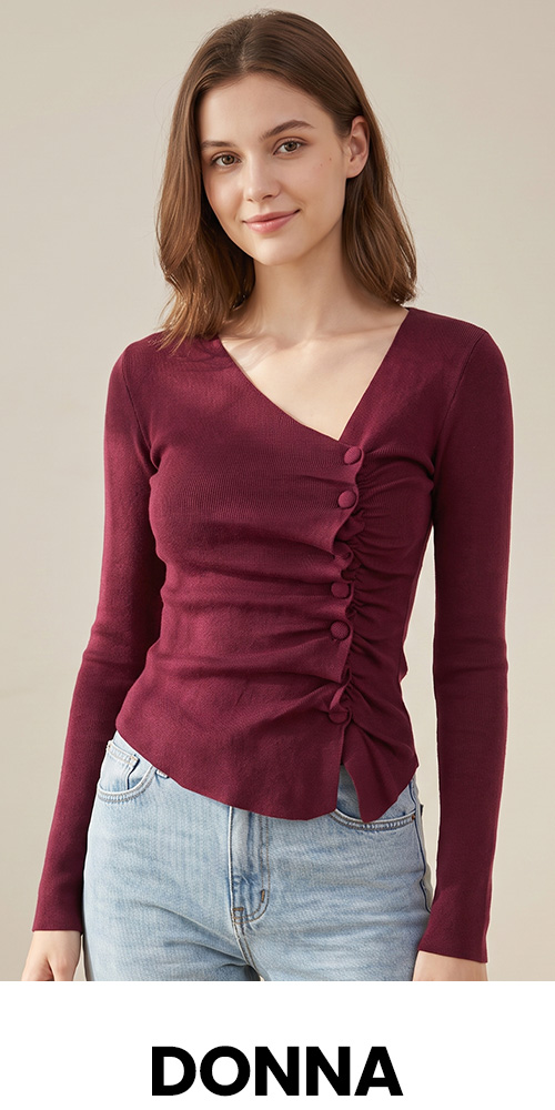 Young woman wearing burgundy ruched buttoned V-neck long-sleeve top and light denim jeans against a neutral background