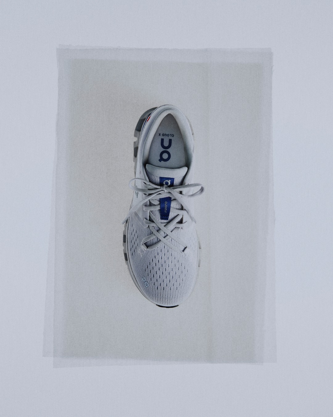 Top view of a white running shoe with breathable mesh upper and tied laces on a pale background