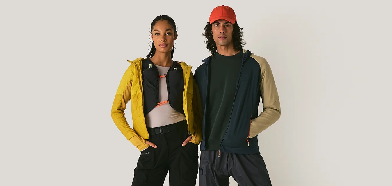 Outfit sportivo: giacca gialla e nera, pantaloni scuri, sneakers colorate, cappellino rosso. Texture distintive e colori a contrasto in tutto.